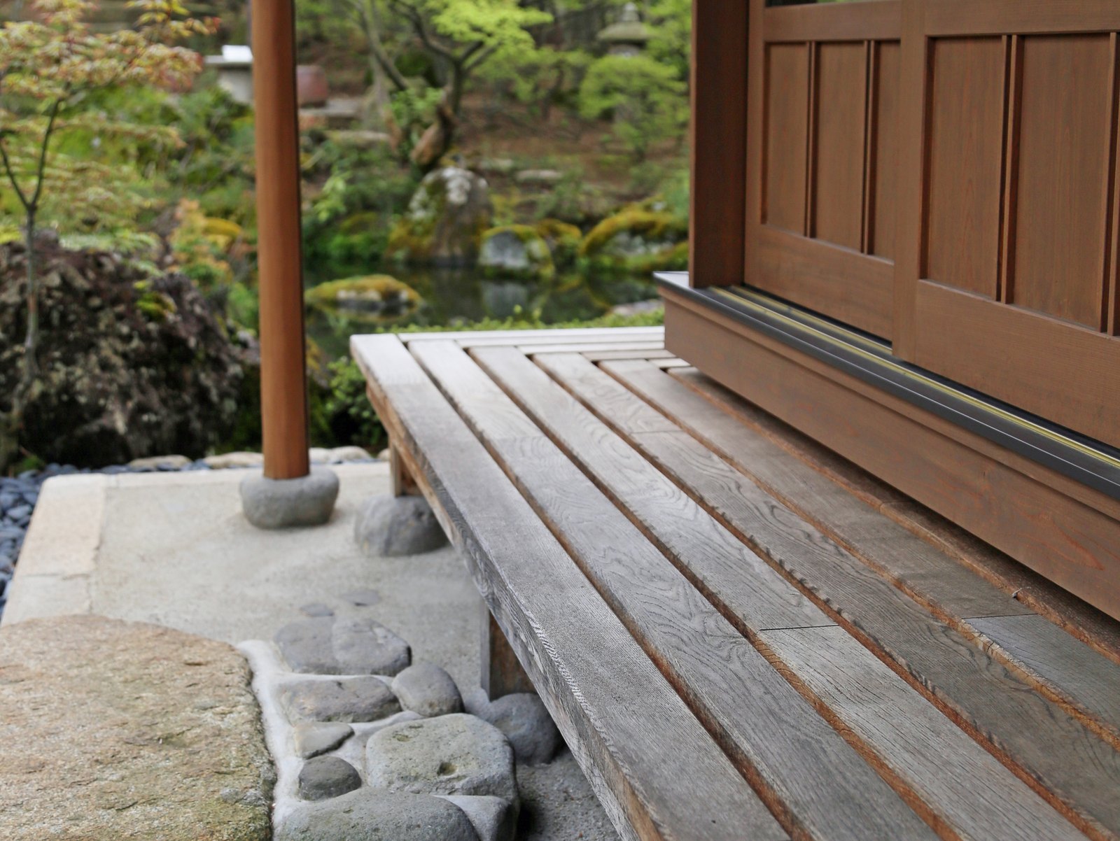 木の濡れ縁と束石、その先に広がる庭の緑と池